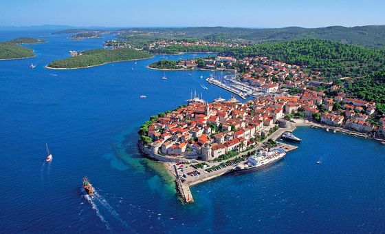 Aerial view of Korčula Old Town on a small peninsula surrounded by deep blue Adriatic Sea, with red rooftops and marina visible