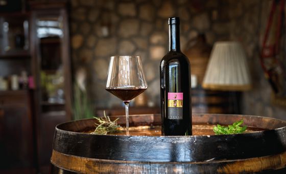 Glass of red wine and wine bottle placed on a wooden barrel inside Lacman Family Winery