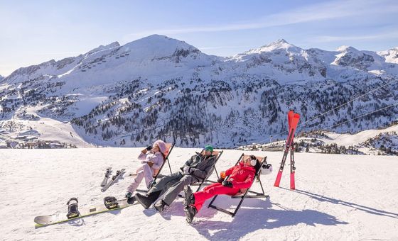 Skiers relaxing on the slopes with snowy mountains in Obertauern.