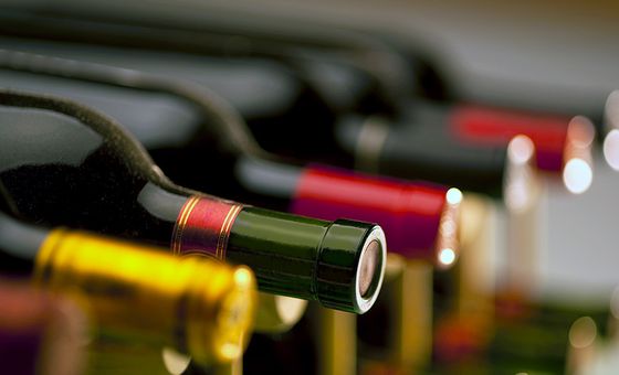Close-up of wine bottles stored horizontally in a rack, with corked ends and colored foil caps in soft focus