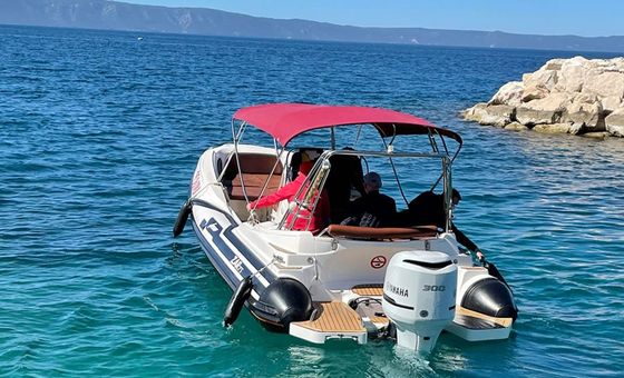 ZAR 75 rigid inflatable boat with red sunshade cruising on bright blue Adriatic sea near rocky coastline on a sunny day